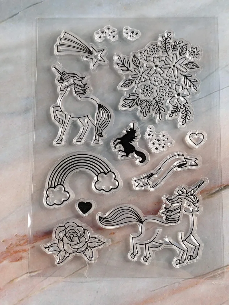 A set of 13 clear cling stamps with outline images of unicorns, rainbows, and flowers.