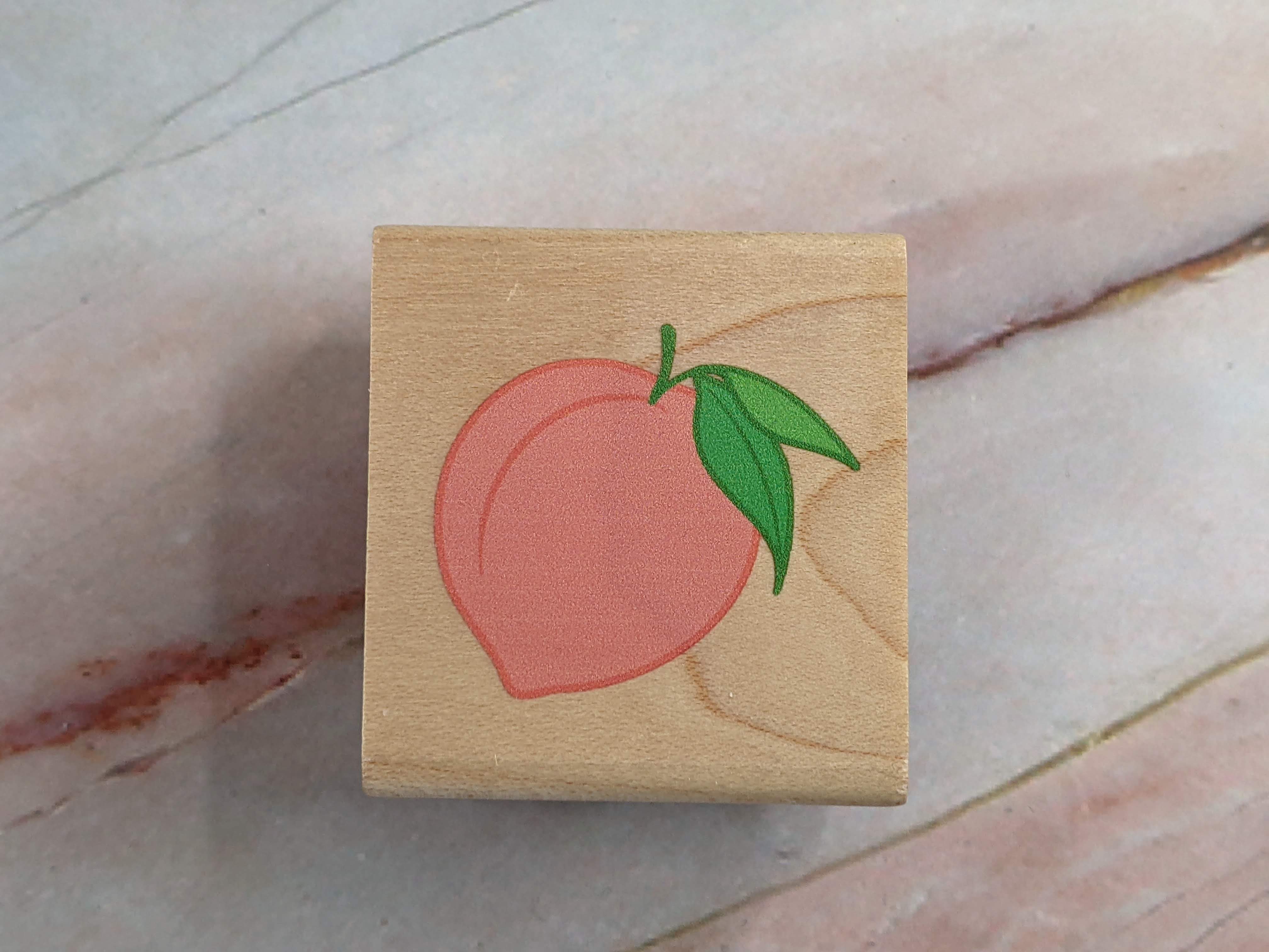 A rubber stamp with an image of a peach, mounted on a wooden block.