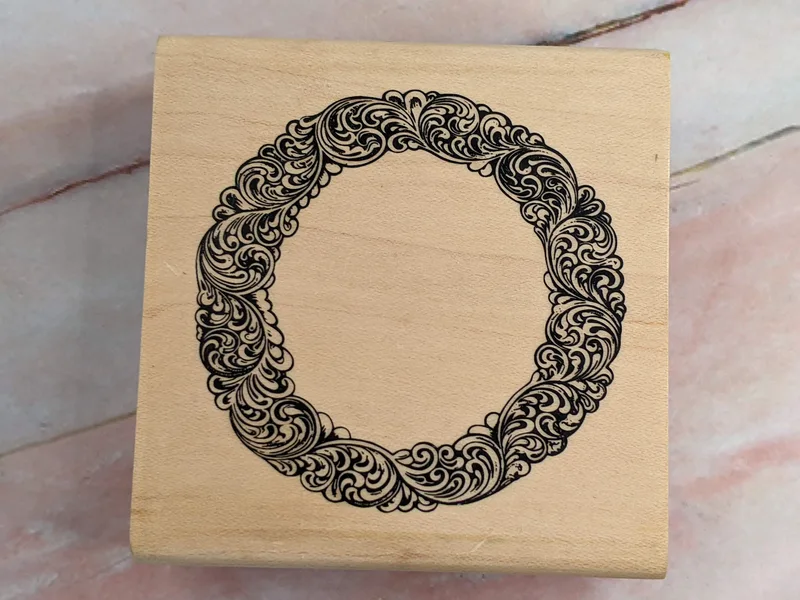 A rubber stamp on a wooden block with an image of a circular ornate frame.