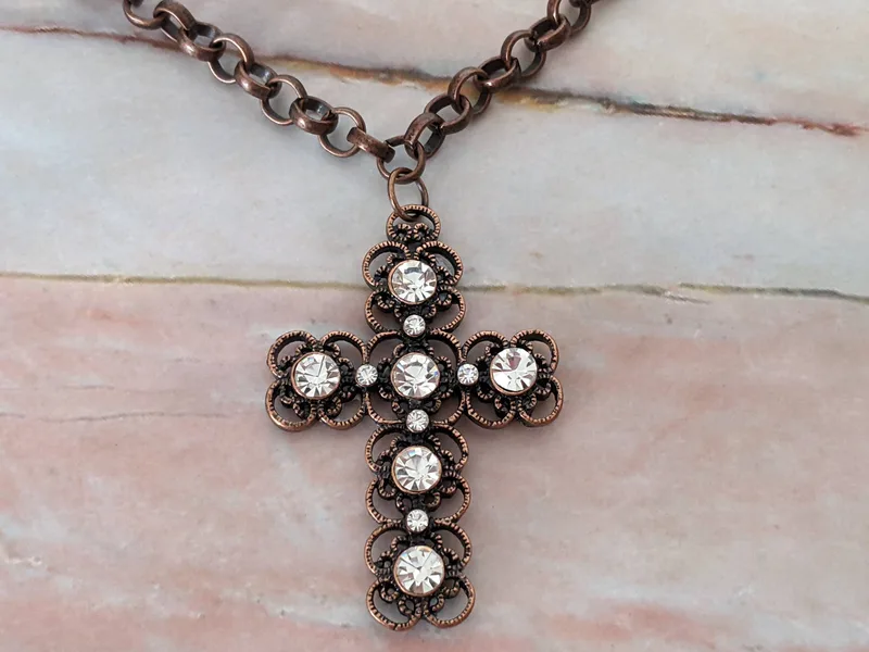 A bronze toned chain necklace with a metal cross pendant that has an inlay of clear gemstones.